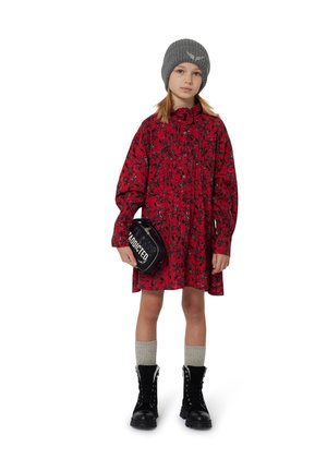 Rode bloemenjurk met een rimpelige kraag, lange mouwen, gecombineerd met een zwarte schoudertas met de tekst "ADDICTED". Draagt grijze sokken en zwarte laarzen.