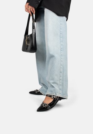 Scarpe nere in pelle a punta con dettagli in metallo, abbinate a jeans ampi blu chiaro e una piccola borsa nera.