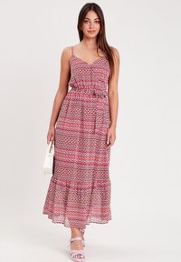 Robe maxi en tissu léger avec un motif géométrique rose et blanc. Elle présente des bretelles fines, une taille cintrée et un ourlet évasé et volants.