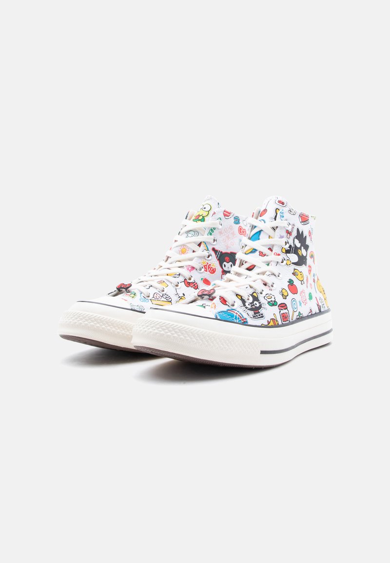 Zapatillas blancas de caña alta con estampados de personajes de dibujos animados coloridos y cordones blancos, exhibidas sobre un fondo gris claro liso.