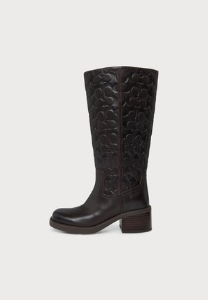 Botte noire en cuir montant jusqu’au genou, ornée d’un motif circulaire en relief, avec des coutures latérales, un bout arrondi et un talon bloc épais.