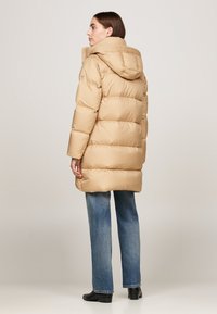 Geacă puffer bej cu glugă, având un design matlasat și o textură lucioasă. Asortată cu blugi din denim albastru deschis și cizme negre până la gleznă.