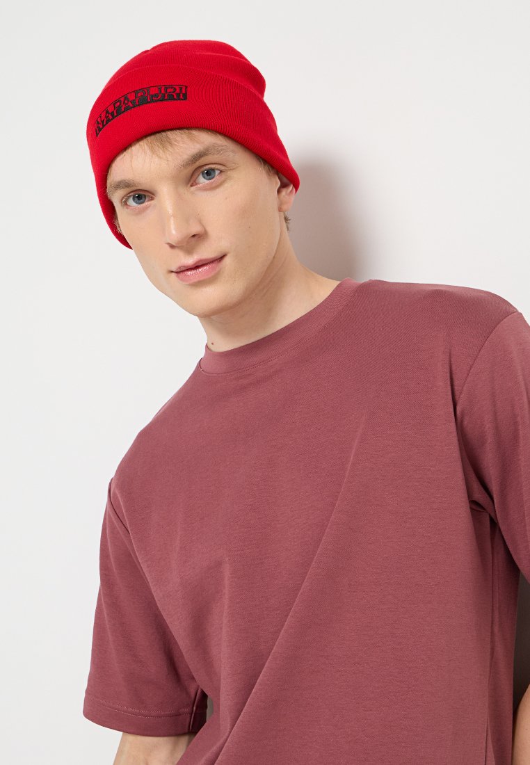 Berretto lavorato a maglia rosso con logo, abbinato a una maglietta a maniche corte di colore mauve e dalla vestibilità ampia. Il berretto ha una texture a coste, mentre la maglietta presenta un collo rotondo.