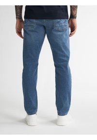 Jasnoniebieskie dżinsy o prostym kroju, z pięcioma kieszeniami oraz subtelnymi detalami szwów na tylnej kieszeni, zestawione z białymi trampkami.