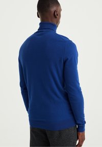 Blå polotröja i mjukt tyg med långa ärmar och en figurnära passform. Ribbad mudd och nederkant fulländar designen.