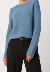 Maglione lavorato a maglia di colore blu chiaro con scollatura a barca e maniche lunghe, abbinato a pantaloni neri e una cintura nera. Tessuto morbido, vestibilità ampia.