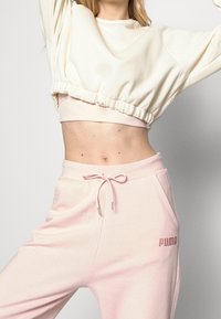 Vit kortärmad sweatshirt med elastisk nederkant och rosa högmidjade joggingsbyxor med fickor och en PUMA-logotyp i ljus broderi.