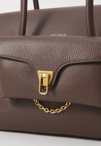 Sac à main en cuir texturé brun avec quincaillerie dorée, poignée supérieure et accent en chaîne. Il dispose d'une fermeture à rabat avec un détail de verrouillage à pression.