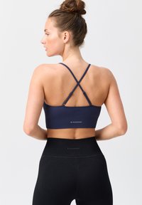 Marinefarbener Rippensport-BH mit überkreuzten Trägern, kombiniert mit hochgeschnittenen schwarzen Leggings. Beide Kleidungsstücke sind mit Logos versehen.