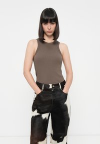 Débardeur marron à côtes associé à un pantalon large en fausse fourrure à motif vache noir et blanc. Le pantalon comporte des poches et des éléments de quincaillerie visibles.