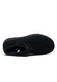 Botín de ante negro con forro de felpa, punta redonda y suela de goma texturizada. Los detalles de costura realzan el diseño general.