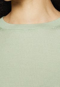 Jasnozielony prążkowany materiał sweterkowy z okrągłym dekoltem, ukazujący miękką teksturę i równomiernie rozmieszczone pionowe linie.