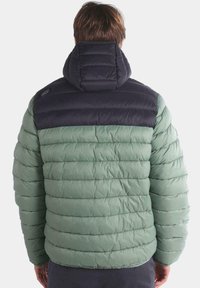 Chaqueta acolchada con una sección superior de color azul oscuro y una parte inferior de color verde claro. Presenta un cuello alto y una textura acolchada en todo su exterior.