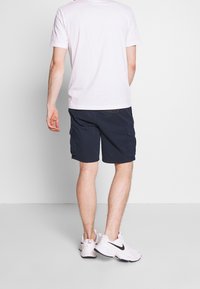 Shorts cargo bleu marine avec deux poches latérales, conçus en tissu mélangé coton, accompagnés d'un t-shirt blanc à col rond et de baskets blanches.