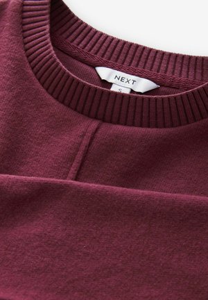Burgundijas krāsas crewneck džemperis ar teksturētu audumu, riboto apkakli un smalku vīlēm. Zīmola etiķete "NEXT" redzama iekšpusē apkakles.