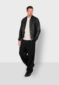 Černá kožená bomber bunda s žebrovanými manžetami a límcem, v kombinaci s světle zbarveným tričkem a širokými černými kalhotami. Boty s gumovou podrážkou.