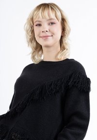 Pulover negru din tricot, cu detalii din franjuri pe o parte, guler rotund și croi lejer. Textură netedă, mâneci lungi.