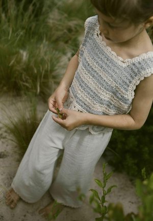 Haut en crochet avec des rayures bleues et crème, encolure festonnée ; associé à un pantalon ample gris clair. L'enfant tient une feuille verte dans les mains.