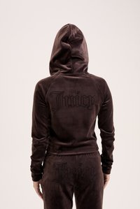 Brun velour træningssæt med hætte, med "Juicy" logo i rhinsten på bagsiden af toppen og bukserne. Glat, struktureret overflade.