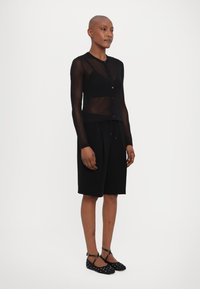 Black sheer long-sleeve cardigan with button closure over a black knee-length skirt, paired with black dotted ballet flats. Smooth texture.