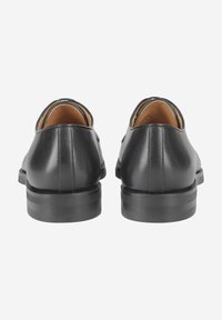 Chaussures en cuir noir avec une finition lisse, des bords arrondis, un talon plat et une semelle intérieure claire contrastante.