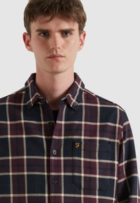 Geruit shirt met een marineblauwe basis, bordeauxrode en witte ruiten, knoopsluiting en een klein geborduurd logo op de borstzak.