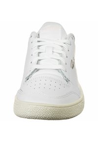 Białe skórzane trampki z perforowanymi detalami na czubku, płaskimi sznurówkami i teksturowaną gumową podeszwą. Złote logo po boku.