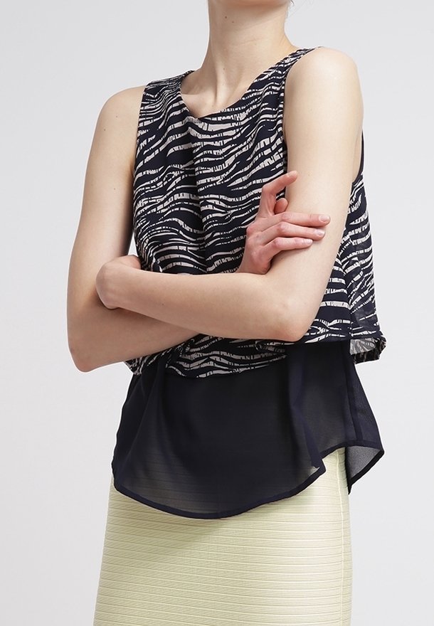 Top senza maniche di colore blu navy con strisce astratte bianche, design a strati e orlo trasparente. Tessuto morbido, vestibilità rilassata e scollatura rotonda.
