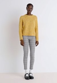 Pull jaune en peluche, pantalon ajusté à carreaux gris, chaussettes blanches et chaussures noires. Tricot texturé, encolure ronde et silhouette de jambe slim.