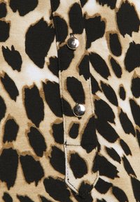 Látka s leopardím potiskem v odstínech hnědé a černé. Obsahuje kovové patentky podél vertikálního zapínání, které zvýrazňují texturované designové detaily.