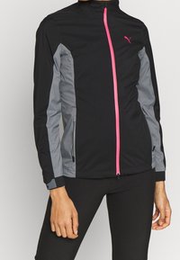 Svart sportjacka med grå sidopaneler och en ljusrosa dragkedja. Har dragkedjefickor och en hög krage. Lätt material.