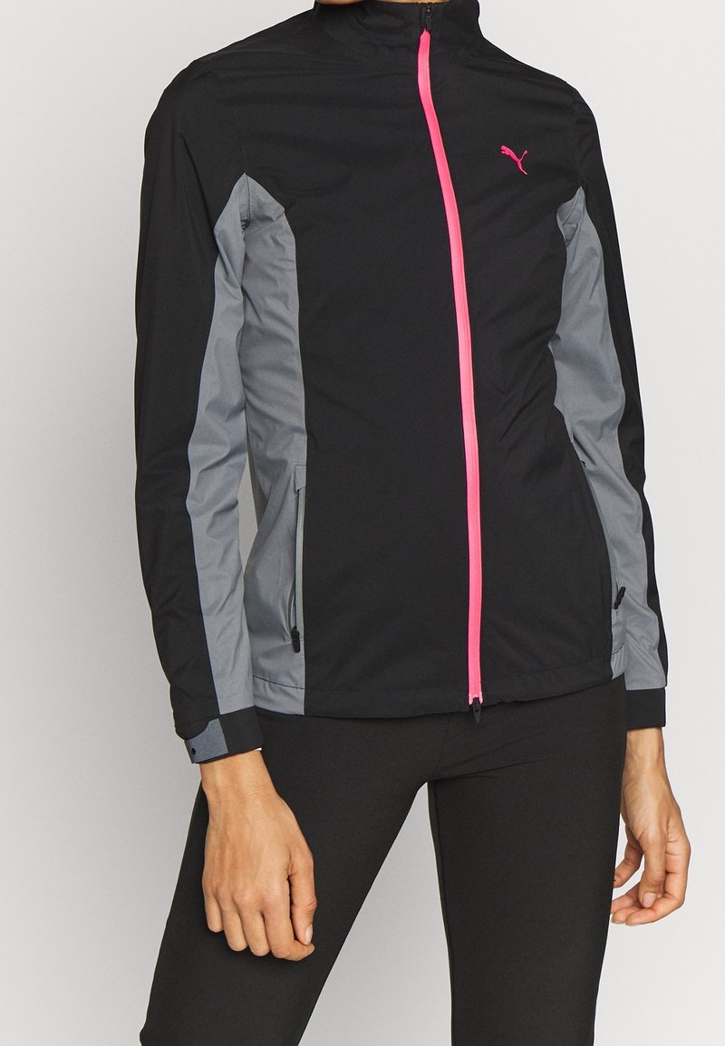 Svart sportjacka med grå sidopaneler och en ljusrosa dragkedja. Har dragkedjefickor och en hög krage. Lätt material.