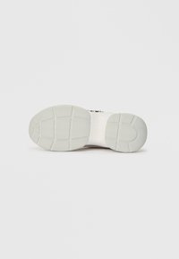 Bijela sneaker potplat s teksturiranim gumenim uzorkom za prijanjanje. Sadrži naziv branda "GUESS" utisnut na sredini. Minimalistički dizajn.