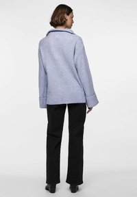 Svetlo vijoličasta rebrasta jopica z velikim ovratnikom in širokimi rokavi, v kombinaciji z črnimi ravnimi hlačami in škornji, prikazana s hrbtne strani.