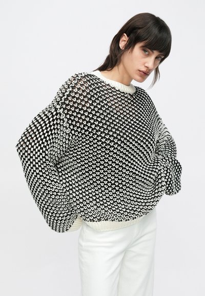 Μαύρο και άσπρο πουλόβερ με πλεκτό μοτίβο, άνετη γραμμή, φαρδιά μανίκια και υφή στην επιφάνεια. Διαθέτει κρεμ ριμπ ζιβάγκο στο γιακά και στο τελείωμα.