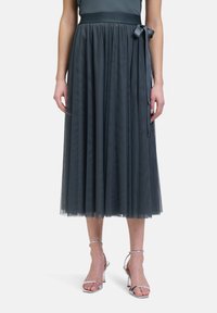 Jupe midi en tulle gris avec une taille froncée et un lien en satin. La jupe a une texture transparente et un design superposé, accompagnée de talons argentés.