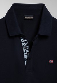 Polo blu navy con tessuto testurizzato, caratterizzato da un pannello stampato bianco all'interno del colletto e un piccolo emblema a bandiera rossa e bianca.