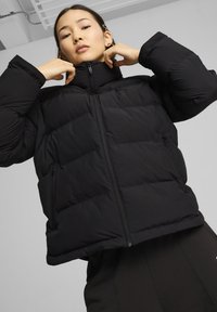 Sort puffjakke med høj krave, lynlåslukning foran og sidelommer. Designet har en quiltet tekstur og en cropped silhuet.