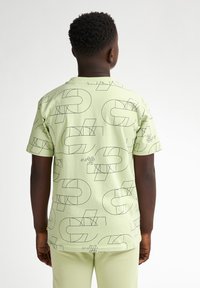 Lichtgroene T-shirt met zwarte geometrische patronen, korte mouwen en een ronde hals. Gemaakt van zacht katoen.