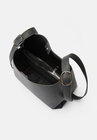 Sac à main en cuir noir de forme arrondie, avec une bandoulière réglable et une poche intérieure zippée. Dispose de quincaillerie en argent et d'une texture lisse.