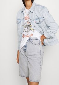 Giacca di jeans azzurro chiaro con vestibilità rilassata, abbinata a una maglietta bianca con grafica e pantaloni corti di jeans grigio chiaro. Design semplice, nessun motivo visibile.