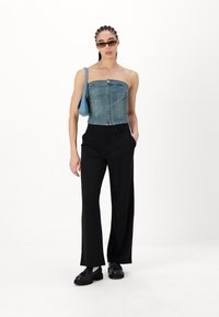 Denim top bez naramenica s prednjim kopčanjem, crne široke hlače visokog struka i crne cipele, u kombinaciji s malom plavom torbicom.