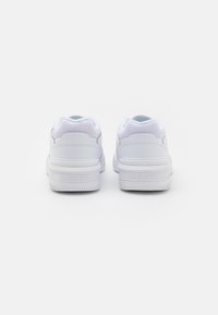 Balti sportbačiai su lygiu odiniu paviršiumi, akių akcentais ant kulno ir tekstūruota guma. Sukurtas su "Lacoste" logotipo uždange.