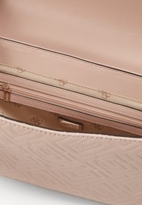 Innenseite einer pinken Handtasche mit strukturiertem Material, einem Reißverschlussfach und Logodetails. Geometrisches Muster auf der Außenseite geprägt. Aus glattem Leder.