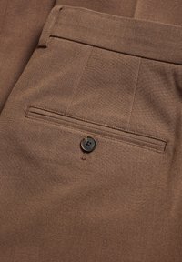 Bruna skräddarsydda byxor i texturerad tyg, med en bakficka med en svart knapp och stickade detaljer.