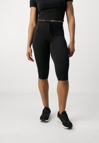 Conjunto atlético negro que incluye una camiseta corta ajustada y leggings capri de talle alto, con una textura suave y cintura ajustable con cordón.
