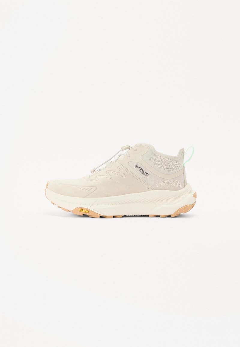 Lys beige treningssko med en teksturert syntetisk overdel, polstret såle og gummisåle for godt grep. Funksjoner inkluderer et snørelukking og logo.