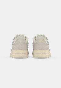 Pair of light gray and beige sneakers with suede heel detail and "Tommy Jeans" embossed on the back sole, viewed from behind.
