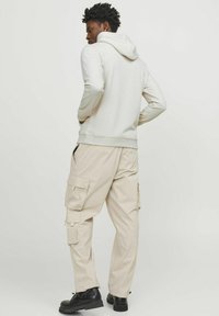 Lys grå hættetrøje med snoretræk, sammen med beige cargo bukser med flere lommer. Modellen bærer sorte støvler.
