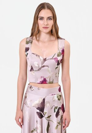 Femme portant un crop top lavande sans manches et une jupe taille haute assortie avec un grand motif floral dans des tons violets et verts.